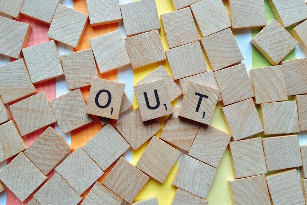 Scrabble tiles spelling 'out' on a rainbow background