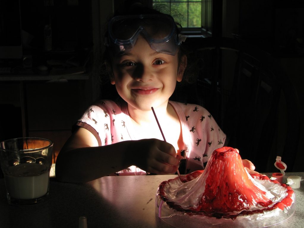 A little girl in goggles painting a volcano model
