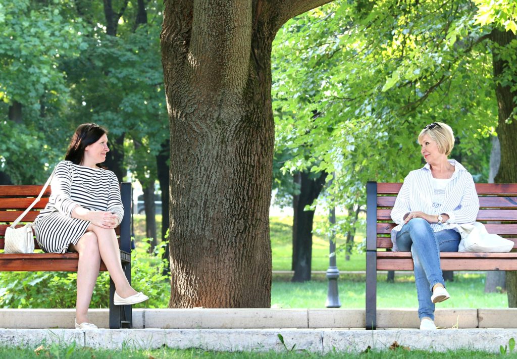 Two women sitting on different park benches, looking at each other