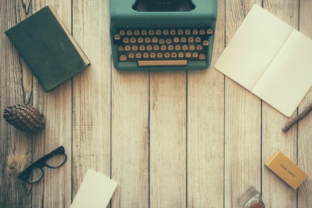 Typewriter on a desk with notepad and writing implements